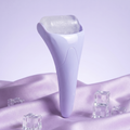 Purple ice roller standing on lilac silk with ice cubes